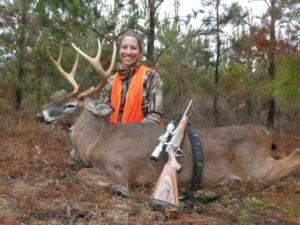 A woman posing with a giant, typical whitetail deer taken with a rifle.